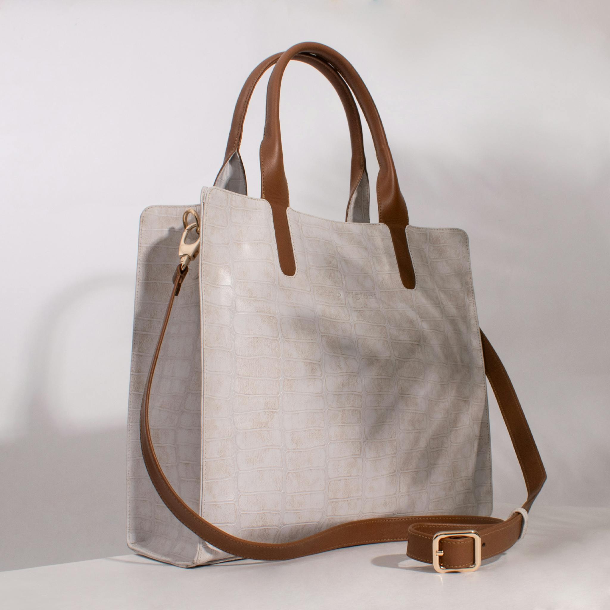 Luxury beige leather handbag with brown straps in a studio setting, showcasing elegance and texture.