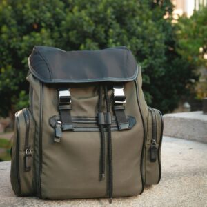 Modern olive green backpack with leather details sitting outdoors on stone. Perfect for travel or fashion look.